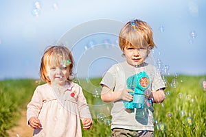 Toddler girl and blond boy brother play with soap bubble gun
