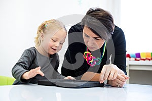Toddler girl in child occupational therapy session doing playful exercises on a digital tablet with her therapist.