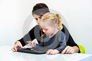 Toddler girl in child occupational therapy session doing playful exercises on a digital tablet with her therapist.