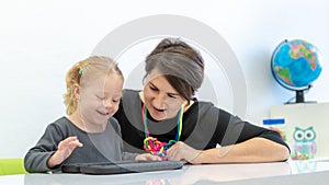 Toddler girl in child occupational therapy session doing playful exercises on a digital tablet with her therapist.