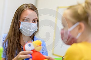 Toddler girl in child occupational therapy session doing playful exercises with her therapist during Covid - 19 pandemic.
