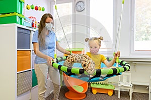 Toddler girl in child occupational therapy session doing playful exercises with her therapist during Covid-19 pandemic.