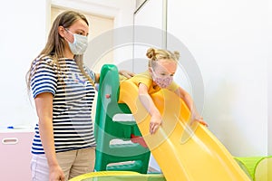 Toddler girl in child occupational therapy session doing playful exercises with her therapist during Covid-19 pandemic.