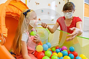 Toddler girl in child occupational therapy session doing playful exercises with her therapist wearing face masks.