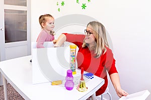 Toddler girl in child occupational therapy session doing sensory playful exercises with her therapist.