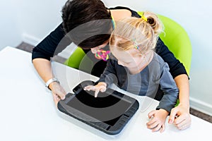 Toddler girl in child occupational therapy session doing sensory playful exercises with her therapist using digital tablet. photo