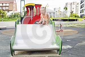Toddler girl on children's slide at playground in summer time. Educational playground equipment