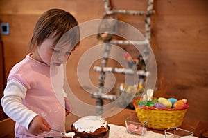 Toddler girl concentrated on decorating Orthodox Easter cake with eggwhite whip
