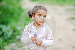 Toddler girl with curly hair playing with yellow dandelions in