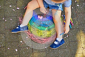 Toddler girl drawing rainbow with colorful chalks on asphalt