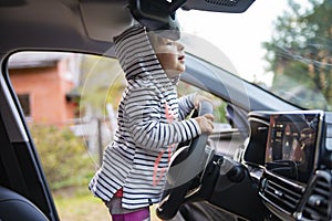 Toddler girl driving a modern car. cute baby holds steering wheel