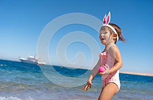 Toddler girl with easter eggs on the beach