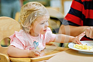 Toddler girl eating healthy vegetables and unhealthy french fries potatoes. Cute happy baby child taking food from