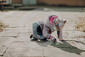 Toddler girl in a facial mask painted on the asphalt with a chalk, playing alone outdoor