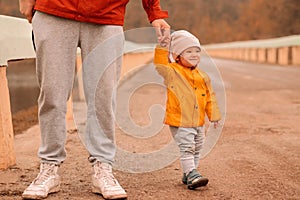 Toddler girl with funny tricky face holding hand of dad on outdoor walk in autumn day. Happy childhood