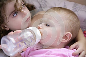 Toddler girl giving bottle of milk to baby sister