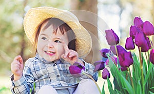 Toddler girl in a hat playing with tulips