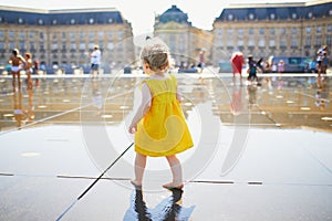 Toddler girl having fun famous outdoor water fountain Miroir d`eau in Bordeaux
