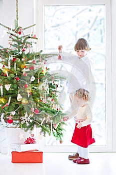 Toddler girl helping her brother to decorate Christmas tree