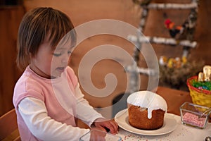 Toddler girl helping mama decorating Orthodox Easter cake with small colorful sugar balls