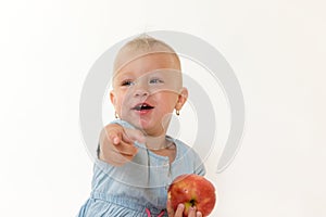 Toddler girl is holding red apple and pointing her finger at the