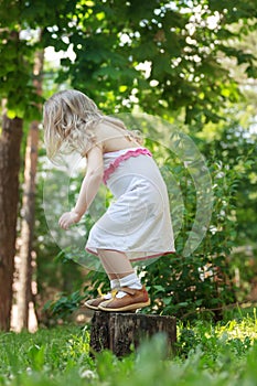 Toddler girl jumping down from tree stump back