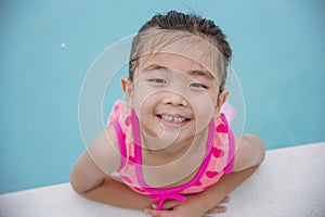 Toddler girl Kid swim playful in swimming pool summer time with pink swimwear in blue water at hotel swimming pool outdoor. Happy