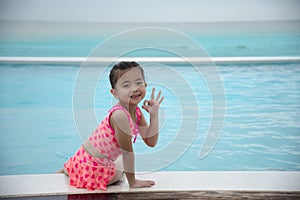 Toddler girl Kid swim playful in swimming pool summer time with pink swimwear in blue water at hotel swimming pool outdoor. Happy