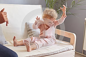 Toddler girl laughing having fun sitting on sofa in living room. at home, adorable little baby raised arms playing. Happy