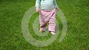 Toddler girl learns to walk barefoot on meadow grass