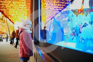 Toddler girl looking at window glass of large department store decorated for Christmas