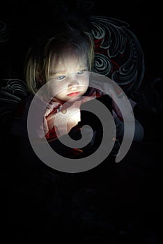 Toddler girl lying on bed and looking on smarthphone screen at night