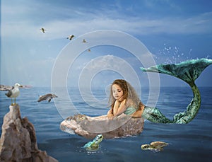 Toddler girl mermaid relaxes on rock in ocean