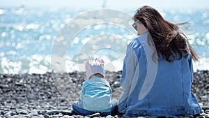 Toddler girl and mother sitting together on pebble beach