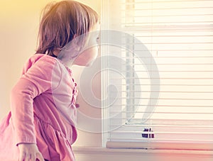 Toddler girl peeking out of the window