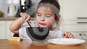 toddler girl picky eater at home kitchen. learning o eat with spoon. bad table manners of kid