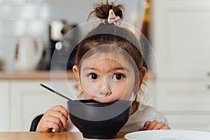 toddler girl picky eater at home kitchen. learning o eat with spoon. bad table manners of kid photo