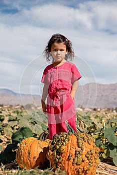 Toddler girl in pink jumpsuit in pumpkin patch field on fall day, childhood memories