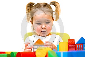 Toddler girl is playing with colorful wooden blocks over white background. Toddler is building a house out of blocks.