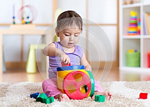 Toddler girl playing indoors with sorter toy sitting on soft carpet