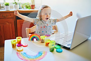 Toddler girl playing modelling clay in front of laptop