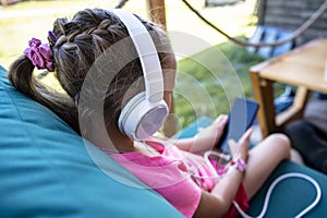 Toddler girl sitting in cafe with headphones and mobile phone in her hands playing games