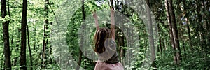 Toddler girl standing in a forest with her arms raised in victorious gesture