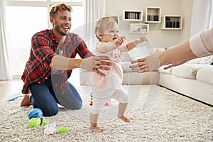 Toddler girl walking from dad to mumï¿½s arms in sitting room