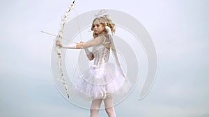Toddler girl wearing angel costume white dress and feather wings. Angel child girl with curly blonde hair. Little angel