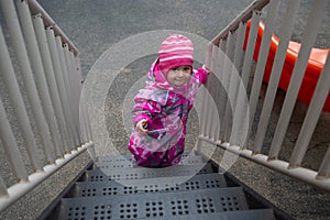 Toddler girl in winter coat Climbing Up Stairs of Outdoor Playground