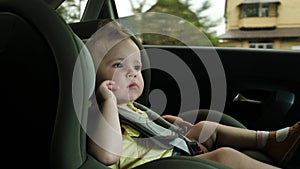 Toddler girl yawns in dark green child car safety seat