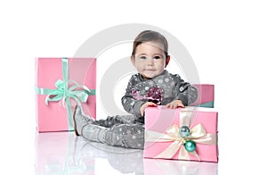 Toddler in gray suit and boots. She smiling, posing with pink decorated gift boxes, sitting on floor isolated on white. Close up