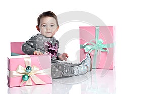 Toddler in gray suit and boots. She smiling, posing with pink decorated gift boxes, sitting on floor isolated on white. Close up