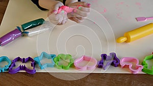 Toddler hands playing colorful play dough with plastic molds and rolling pin